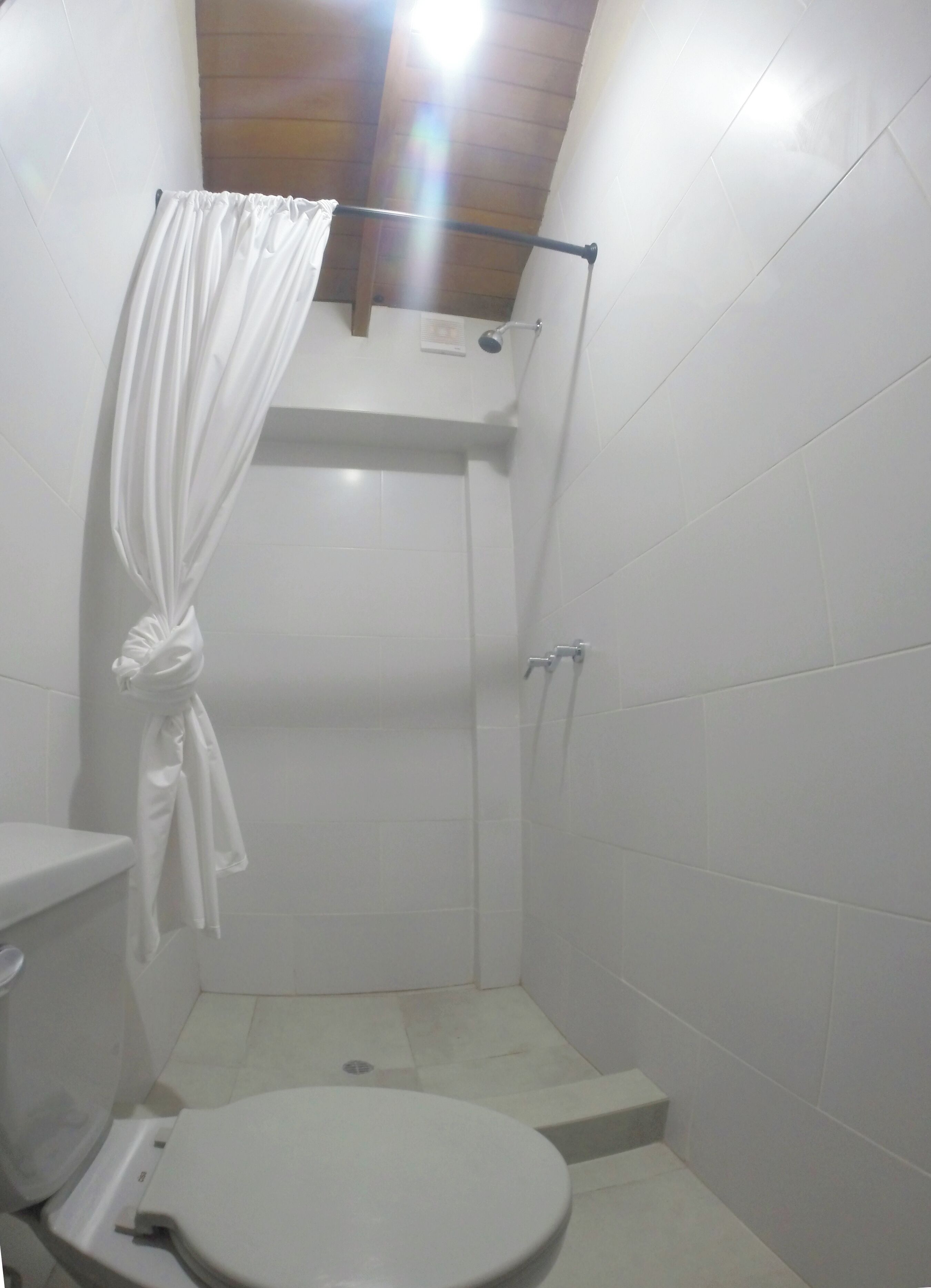 Een kleine, afgesloten douchecel met toilet en een handdoekhouder.