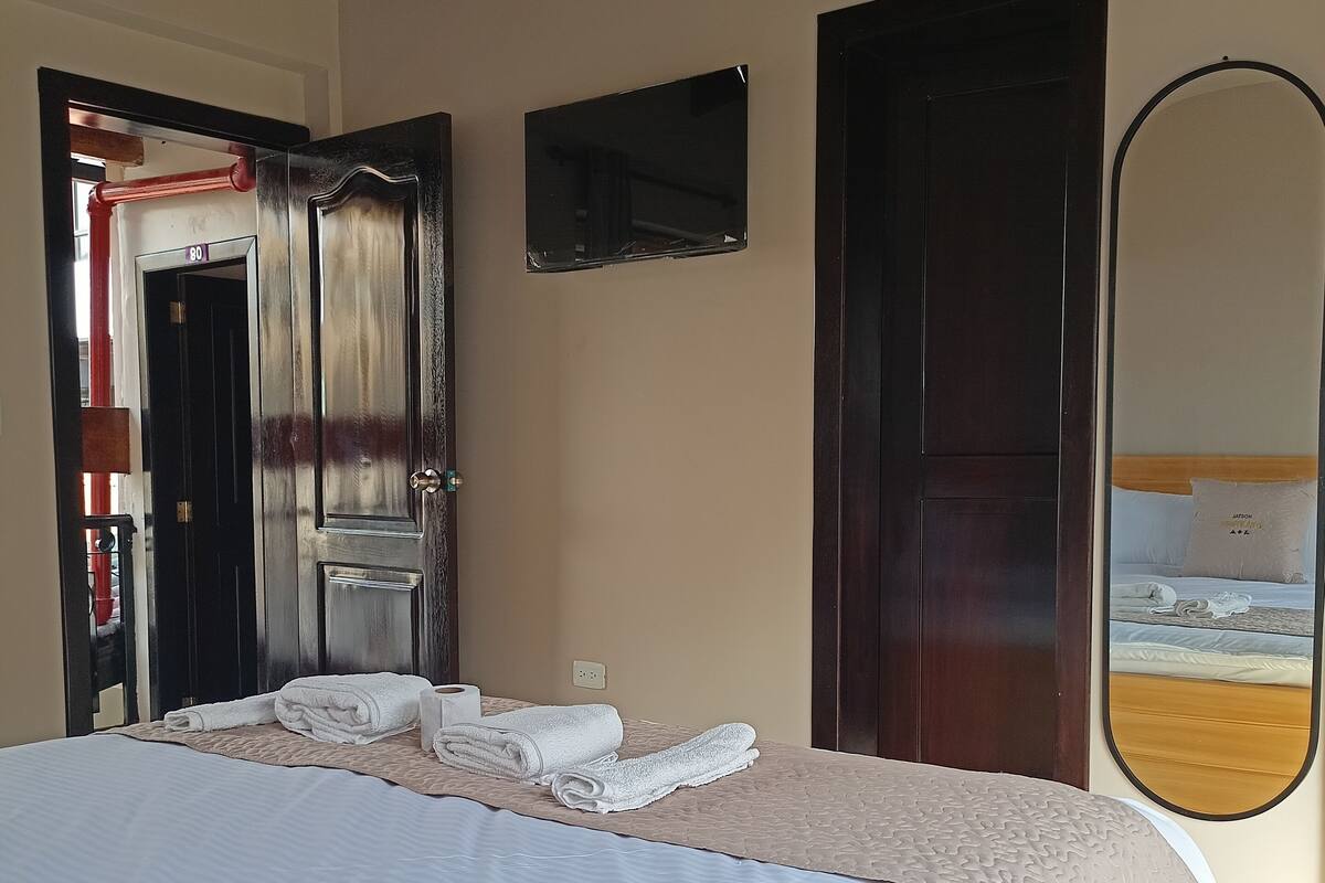 Hotelkamer met een groot bed, een houten plafond, een deur, een spiegel en een uitzicht op een bed in de weerspiegeling.