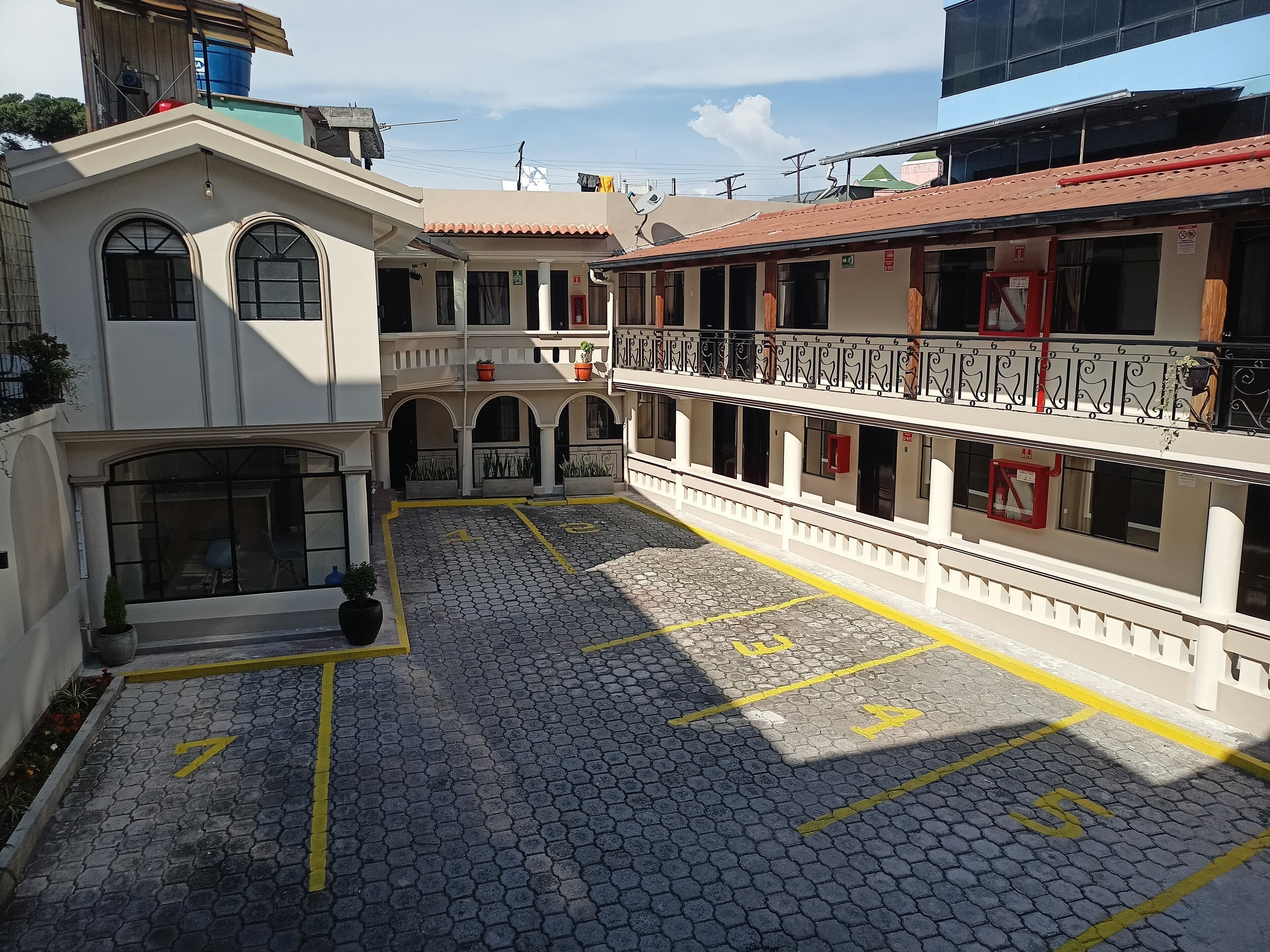 A courtyard with a cobblestone floor, marked parking spaces, and a building with balconies and railings.