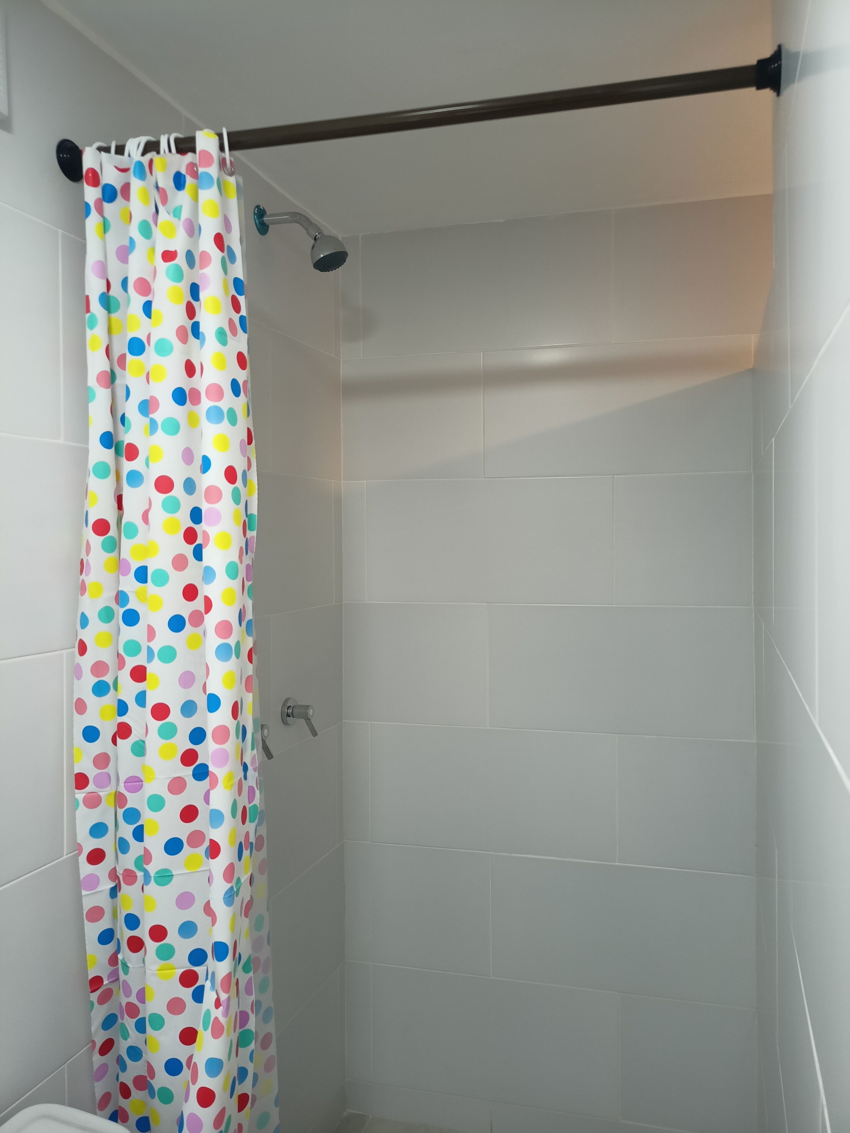 A shower area with white tiled walls and a colorful polka dot shower curtain.
