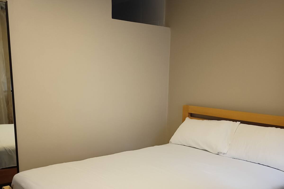 Een netjes opgemaakt bed met een houten frame en witte beddengoed in een kamer met lichte muren en een houten vloer.