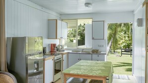 Eine kleine Küche mit Kühlschrank, Herd und Spüle. Ein Tisch mit grüner Tischdecke und Blick auf einen Garten.