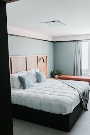 A neatly made bed with a wooden headboard, a bedside table with a lamp, and a potted plant. - Haworth Inn & Conference Center (Holland)