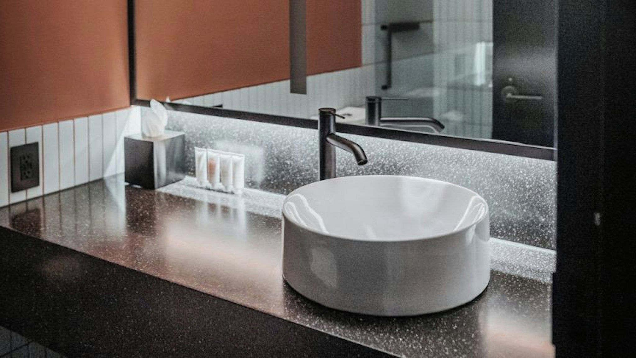 A modern bathroom with a round sink, a towel dispenser, and a mirror.