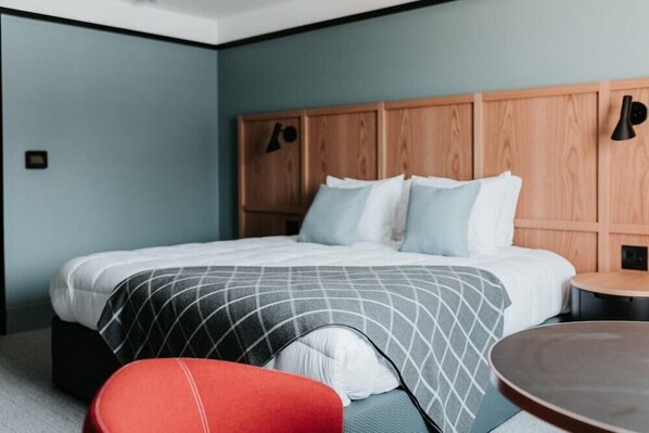 A hotel room with a large bed, a wooden headboard, a red chair, and a small round table. - Haworth Inn & Conference Center (Holland)