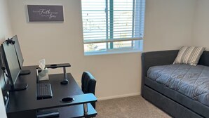 Una camera da letto con una scrivania, un computer e una finestra con persiane.
