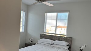 Una camera da letto con un letto in legno, una ventola a soffitto, una finestra con persiane e un comodino con una pianta.