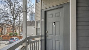 A gray door with a number plate, a balcony with a railing, and a street view with parked cars and buildings in the background. - The Orange Luxe Modern 2bdrm Retreat in Uptown Charlotte ( (Charlotte)