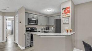 A modern kitchen with grey cabinets, a stainless steel microwave, a built-in oven, and a refrigerator. - The Orange Luxe Modern 2bdrm Retreat in Uptown Charlotte ( (Charlotte)