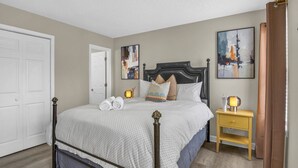 A bedroom with a bed, a nightstand, a door, and two paintings on the wall. - The Orange Luxe Modern 2bdrm Retreat in Uptown Charlotte ( (Charlotte)