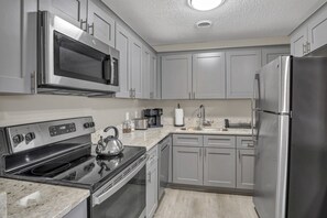 Une cuisine moderne équipée d’appareils électroménagers en acier inoxydable, avec une bouilloire sur la cuisinière et une machine à café sur le plan de travail.
