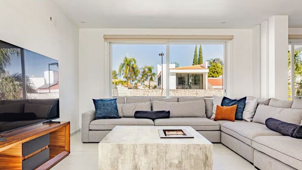 A modern living room with a sectional sofa, a coffee table, and a TV on a wooden stand. - Private Pool • 4BR • 5.5 Baths • Secure • Upscale (Zapopan)