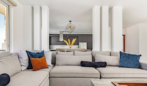 A modern living room with a sectional sofa, a dining area, and a kitchen in the background.