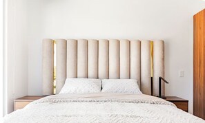 A bed with a textured white cover, a headboard with vertical slats, and a bedside table with a lamp.