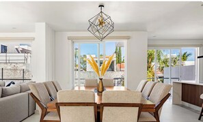 A modern dining area with a geometric chandelier, a dining table with chairs, and large windows offering a view of the outdoors.
