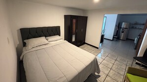 A bedroom with a large bed, a wardrobe, and a kitchenette in the background. - Floral Departments (Comunidad)