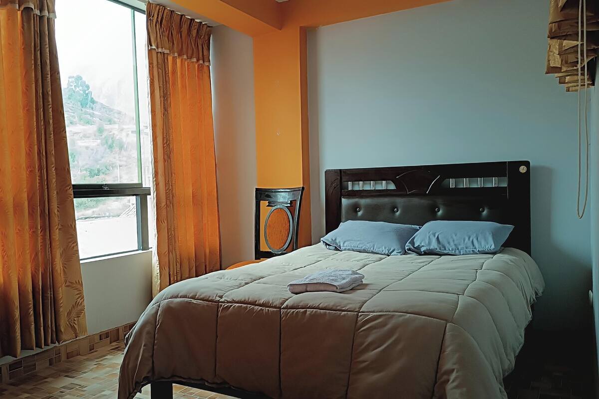 Un dormitorio con cama, cortinas, una silla y ventana.