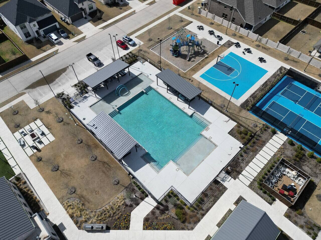 An aerial view of a residential area with a swimming pool, tennis courts, and a basketball court.