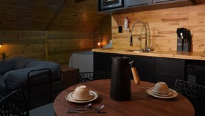 Un intérieur chaleureux, avec des murs en bois, une table à manger dressée pour deux personnes, une cafetière et un canapé en arrière-plan.