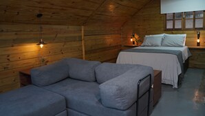 Une chambre confortable dans un chalet en bois, avec un lit, un canapé gris et une petite table.