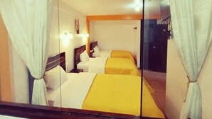 Ett hotellrum med två sängar, vita gardiner och en sänggavel i trä.