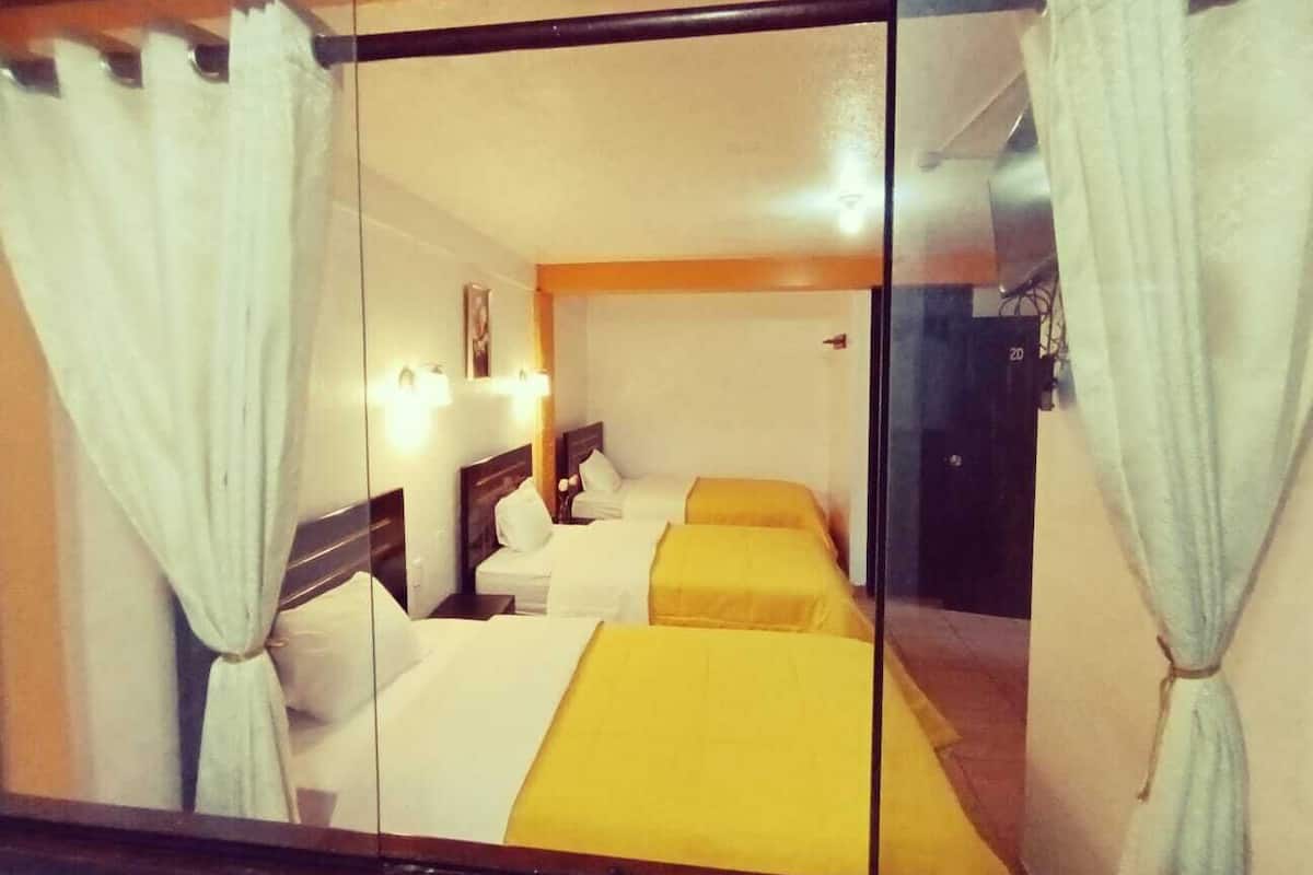 Ein Hotelzimmer mit zwei Betten, weißen Vorhängen und einem hölzernen Kopfteil.