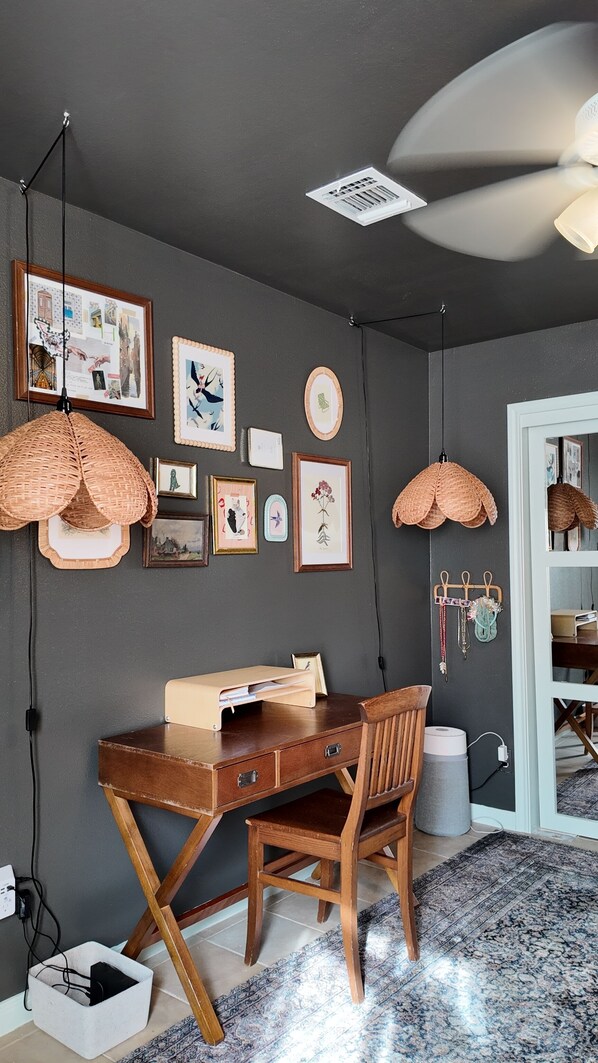 A room with a desk, chair, and various framed pictures on the wall.