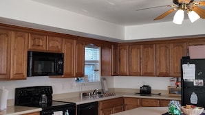 A kitchen with wooden cabinets, a black stove, a microwave, a refrigerator, and a ceiling fan. - Our Coastal Family Home – 2 Blocks to the Beach (Galveston)