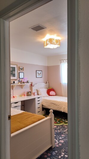 A child's bedroom with a bed, desk, and chair, a ceiling light, and a floral carpet.