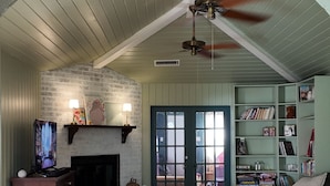 A living room with a fireplace, a television, a ceiling fan, and a bookshelf. - Our Coastal Family Home – 2 Blocks to the Beach (Galveston)