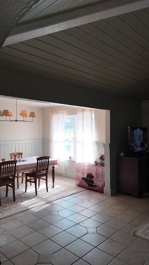 A dining area with a table and chairs, a window with curtains, and a television on a stand.