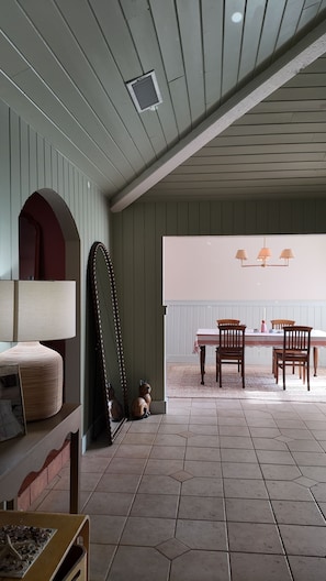 A dining area with a table and chairs, a hanging light fixture, and a large mirror on the wall.
