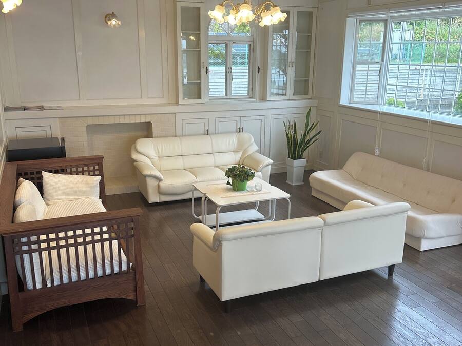 A modern living room with a white sofa, a wooden chair, and a coffee table. There is a chandelier hanging from the ceiling.