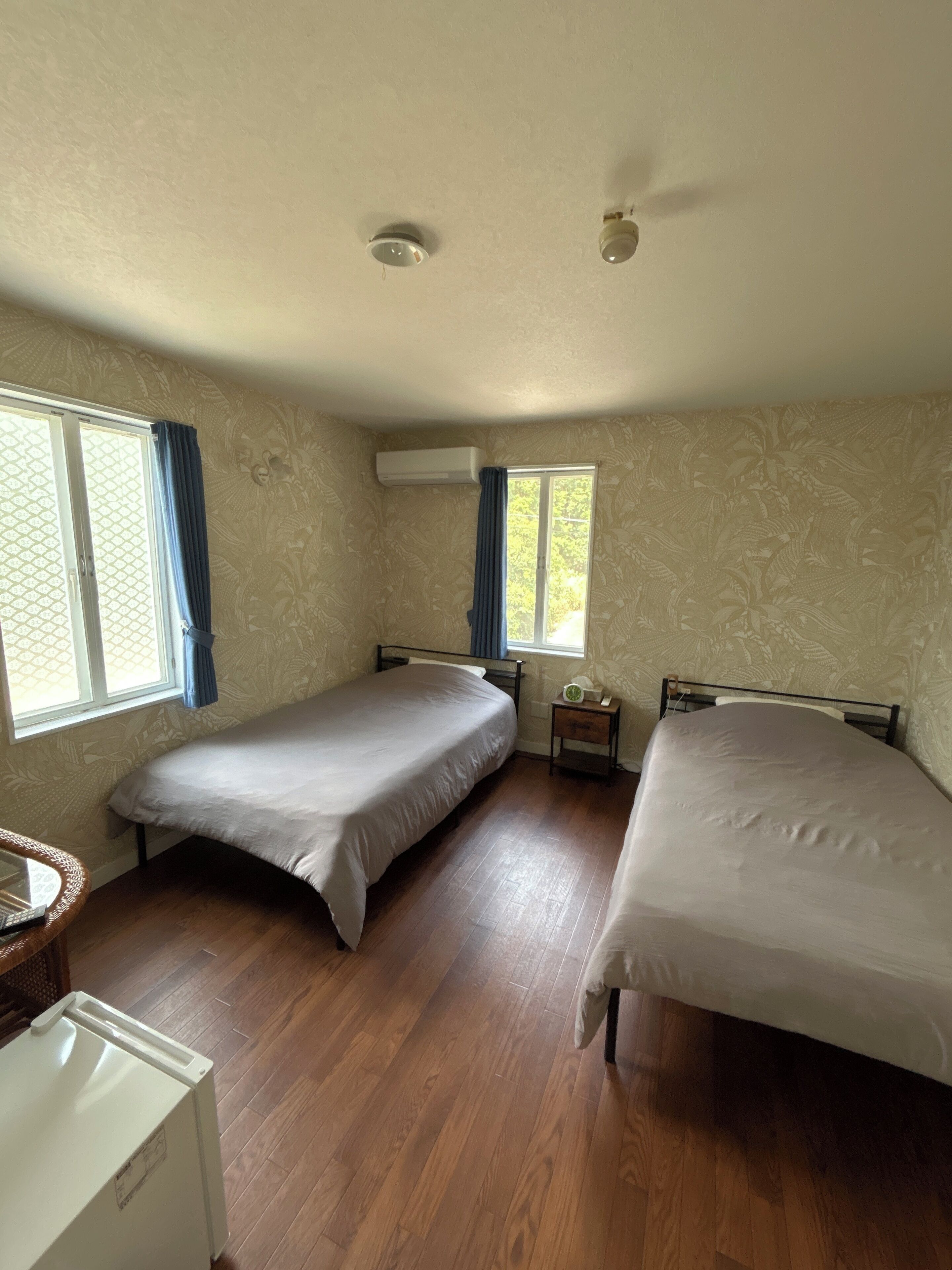 A room with two beds, a small table, a heater, and a window with curtains.