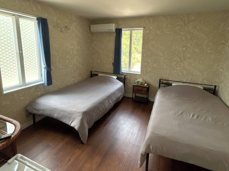 A room with two beds, a small table, a heater, and a window with curtains.