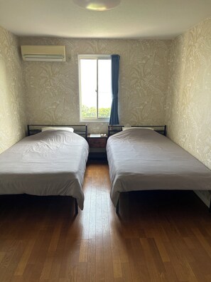 A room with two single beds, a window with curtains, and an air conditioning unit on the wall. - Pension Sora - Hostel (Nachikatsuura)
