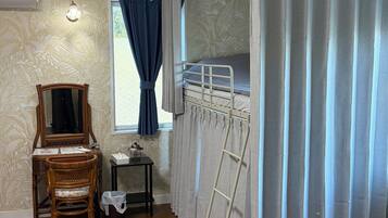 Een kamer met een stapelbed, een stoel, een klein tafeltje, een ladder en een raam met gordijnen.