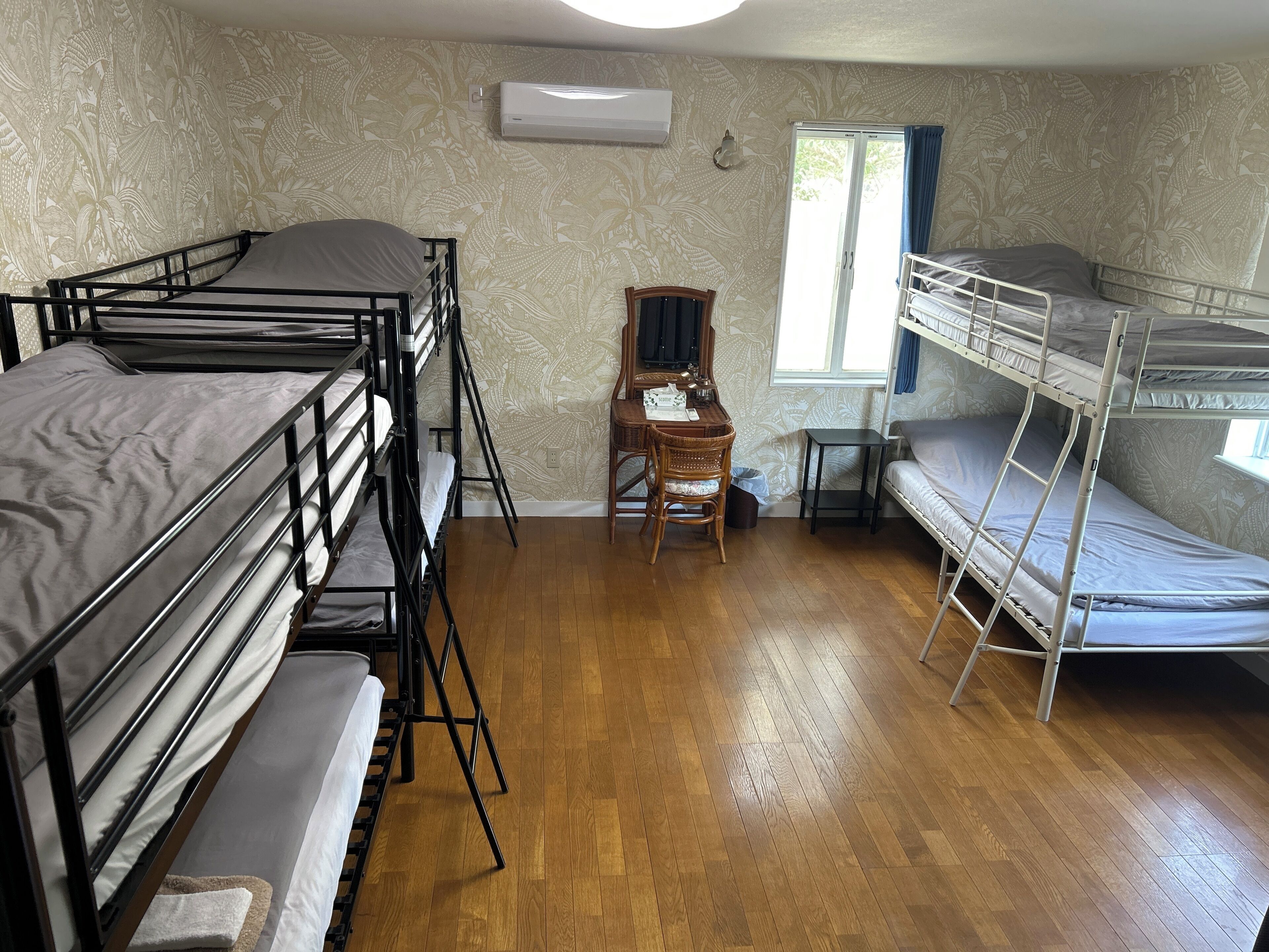 A dormitory room with bunk beds, a desk, and a window.