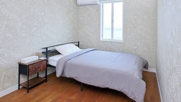 A bedroom with a bed, a nightstand, a dresser, a window, and patterned wallpaper.