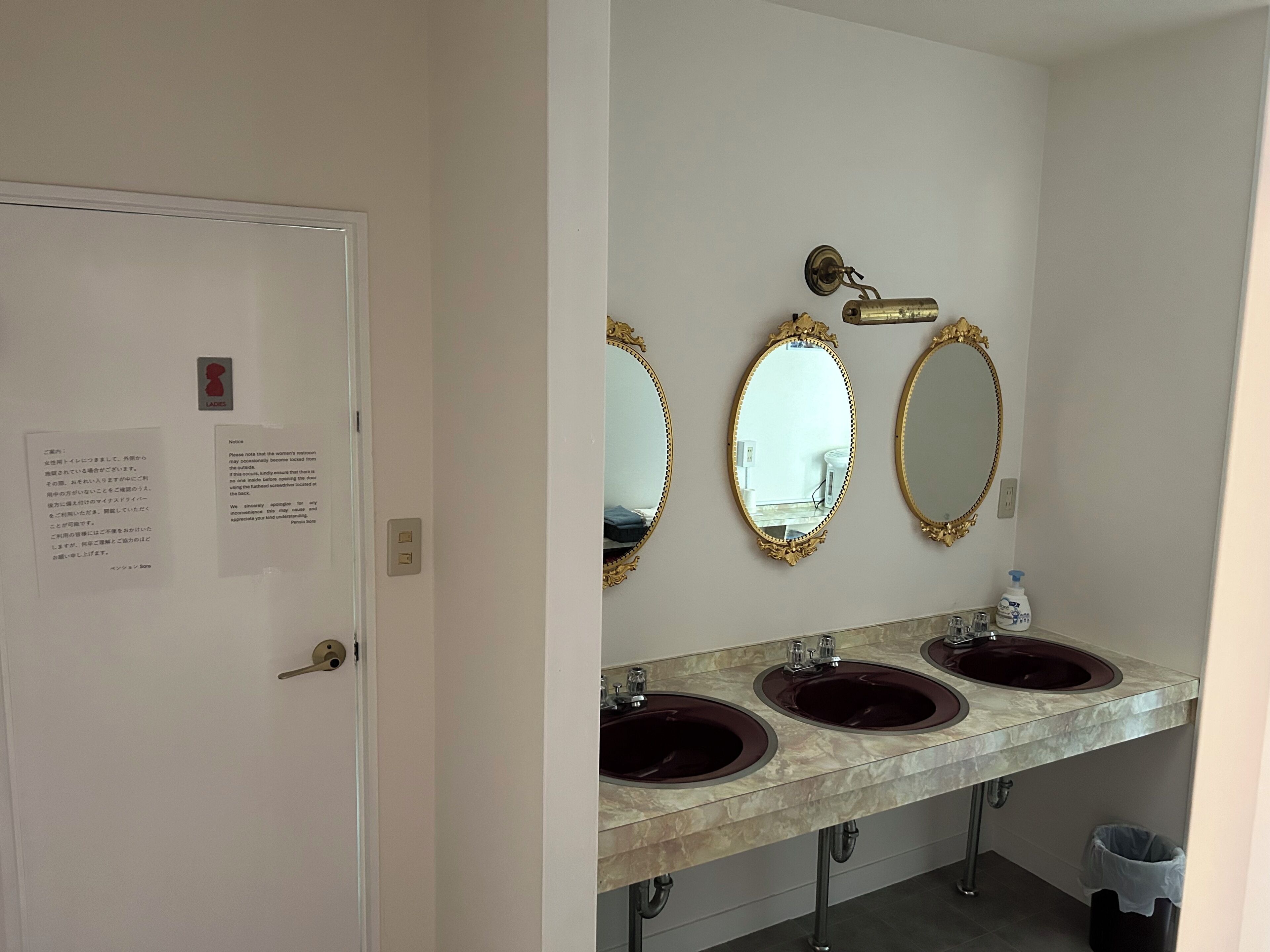 A bathroom with three sinks, a mirror, and a door with a notice.