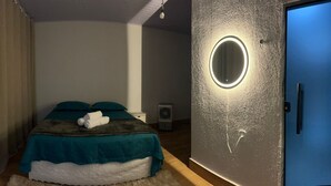 Une chambre à coucher avec un lit, une table de chevet, un miroir fixé au mur et une porte.