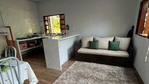 Un espace de vie compact comprenant un coin cuisine, un canapé avec des coussins, une petite table et une chaise.