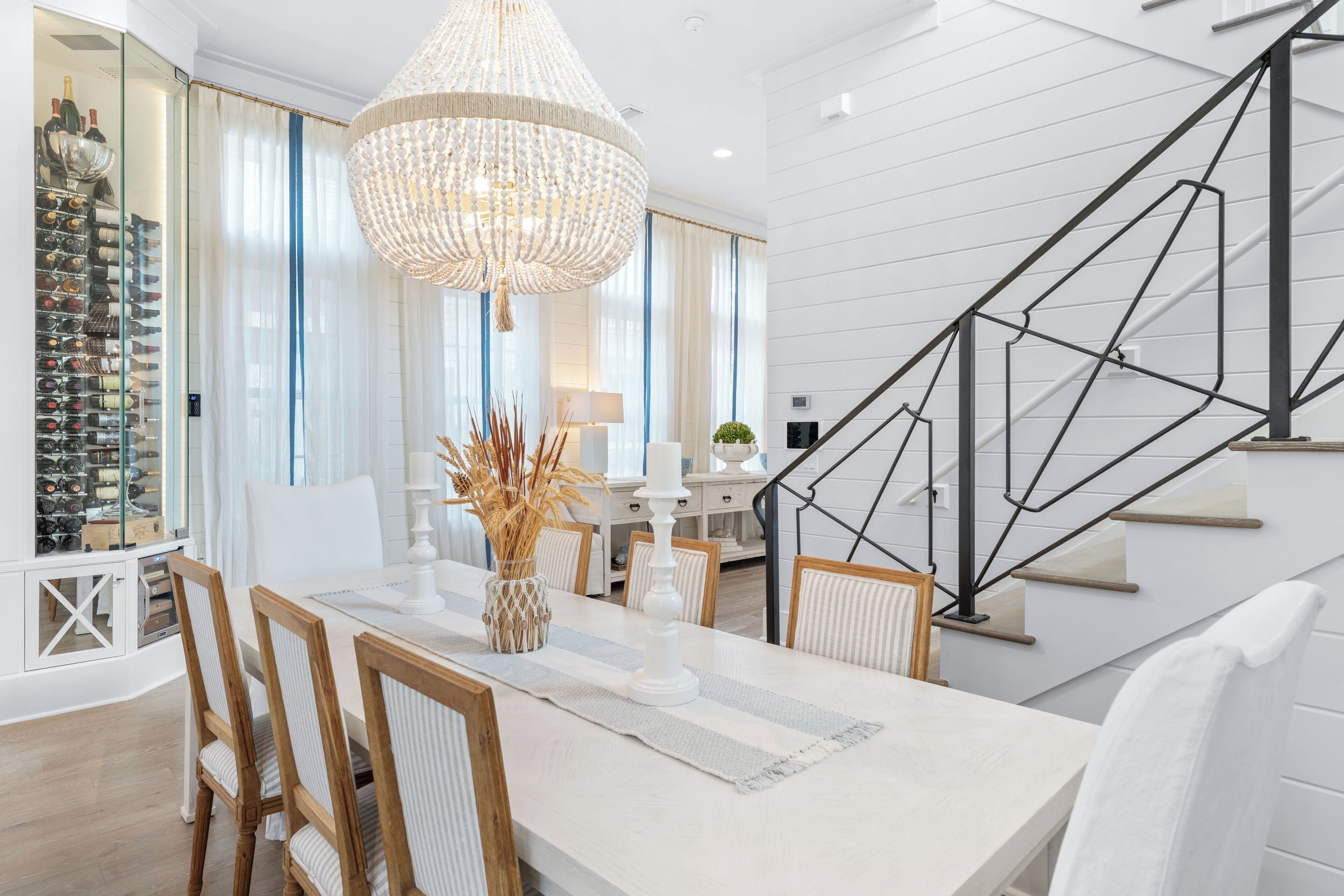 Un espace de salle à manger moderne agrémenté d’un lustre, d’un meuble à vin et d’un escalier.