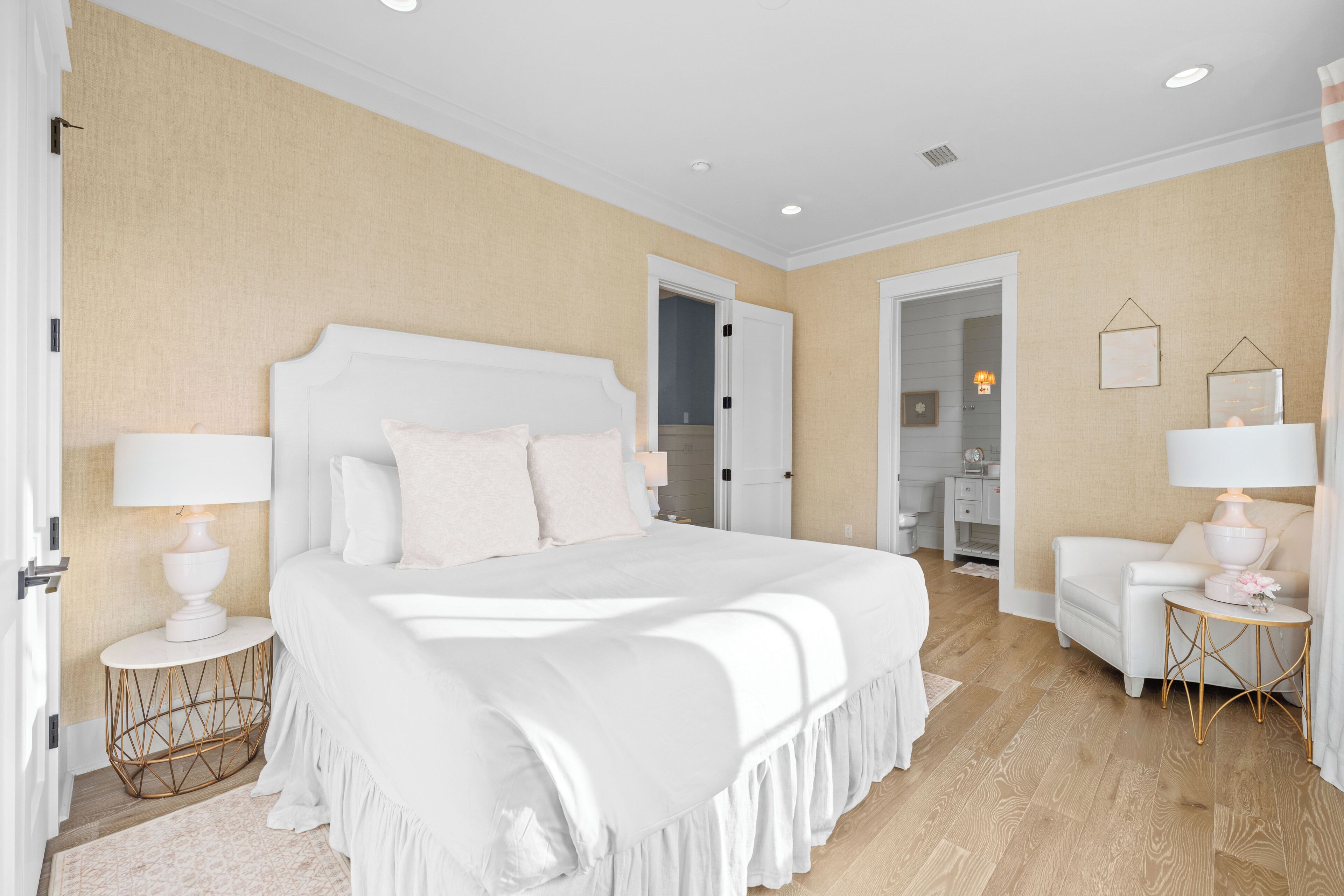 Une chambre d’hôtel avec un grand lit, deux tables de chevet avec des lampes, un petit canapé et une porte donnant sur une salle de bain.