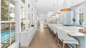 A modern kitchen with a long island, white cabinetry, and pendant lighting. - Camp District Luxury | Private Courtyard Pool | Electric Cart | Beach Club Access (Santa Rosa Beach)