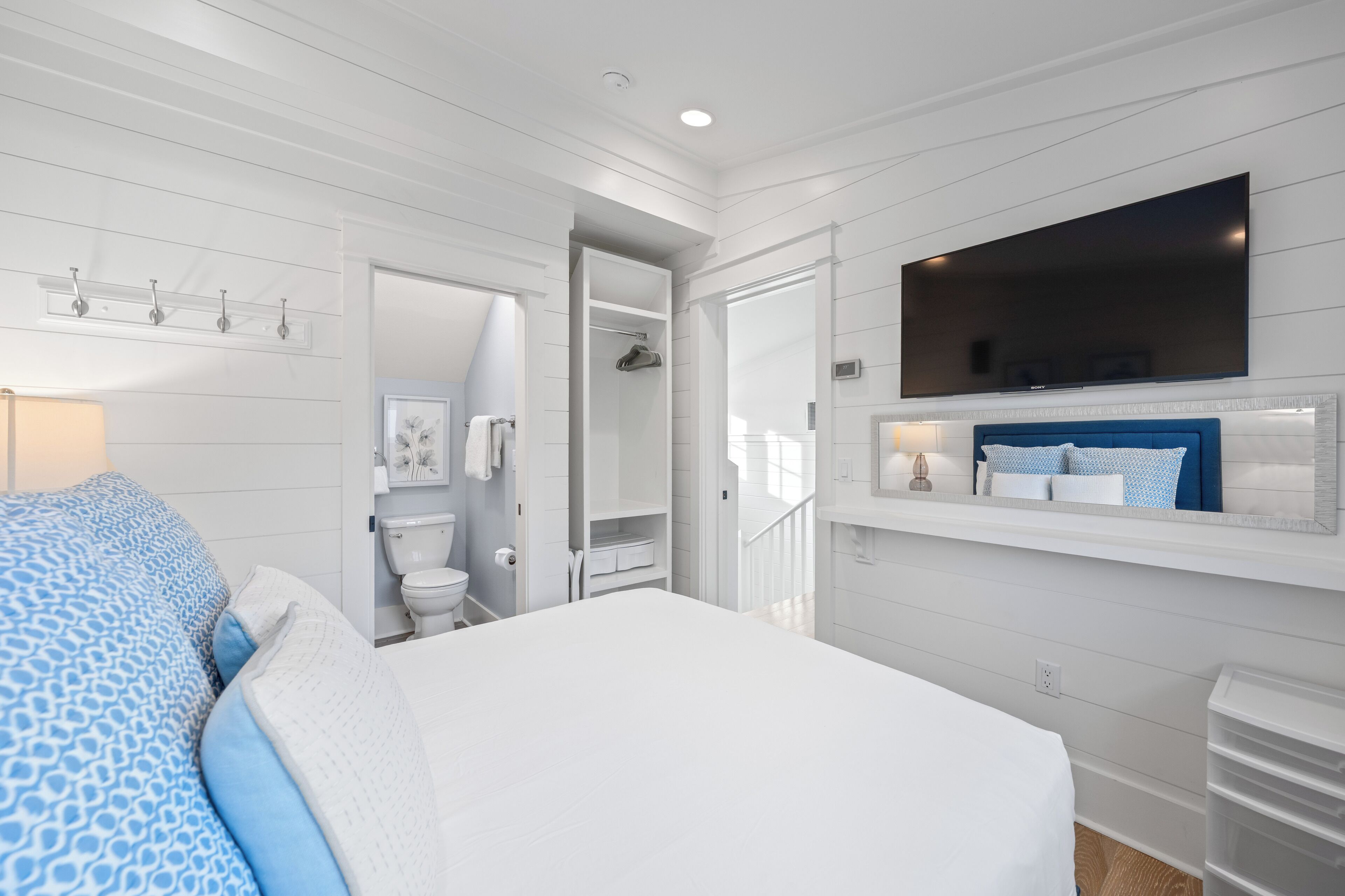 A bedroom with a large bed, a TV mounted above the bed, a walk-in closet, and a bathroom visible through an open door.