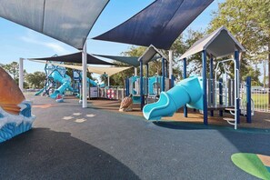 Ein Spielplatz mit Rutschen und Klettergerüsten, beschattet durch große Sonnensegel.