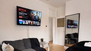 A modern living room with a grey sofa, a black sofa, a bed, and a flat-screen TV displaying Netflix content. - Heart of London Signature Stay | Sleeps 6 (Greater London)