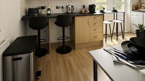 A modern kitchen with wooden cabinets, a stainless steel trash bin, and a bar area with stools. - Heart of London Signature Stay | Sleeps 6 (Greater London)