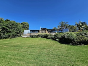 A modern house with a spacious lawn, a wooden deck, and a large tree in the background.